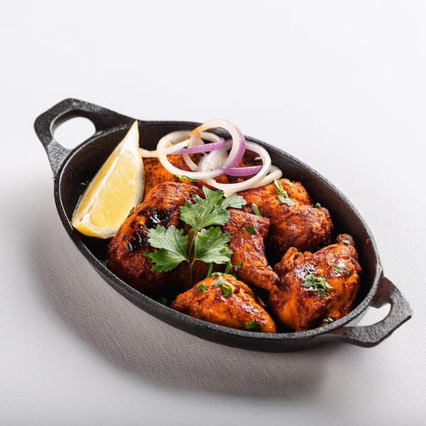 Maharaja Indian Cuisine's Tandoori Chicken in a cast iron skillet, garnished with lemon, onions, and cilantro.