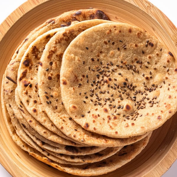 Stack of warm, round Indian flatbreads, some topped with black sesame seeds, on a wooden plate.