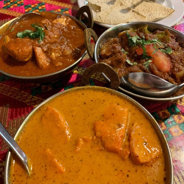 Three bowls of Indian curries, two red and one orange, with a side of papadum.