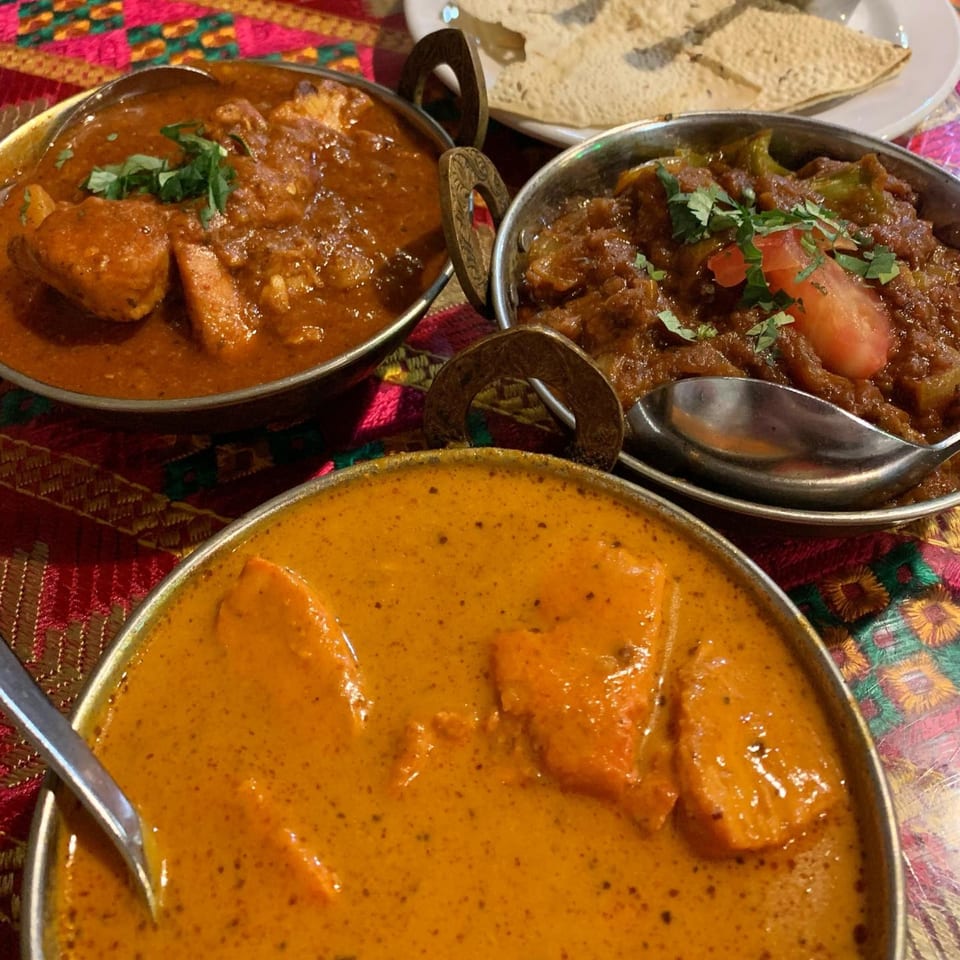 Three bowls of Indian curries, two red and one orange, with a side of papadum.