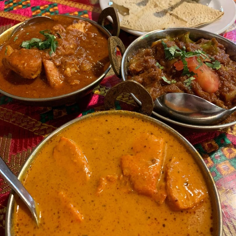 Three bowls of Indian curries, two red and one orange, with a side of papadum.